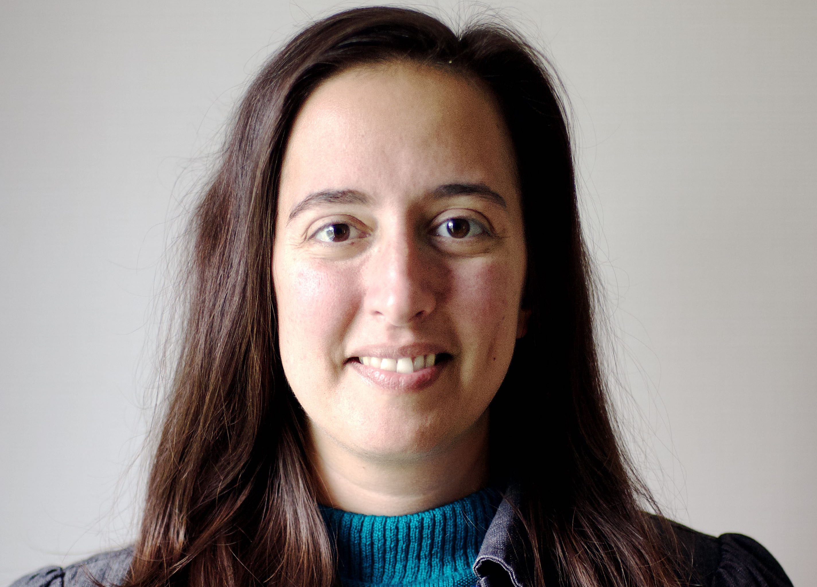 En kvinna i mörkt hår och blå tröja som ler.